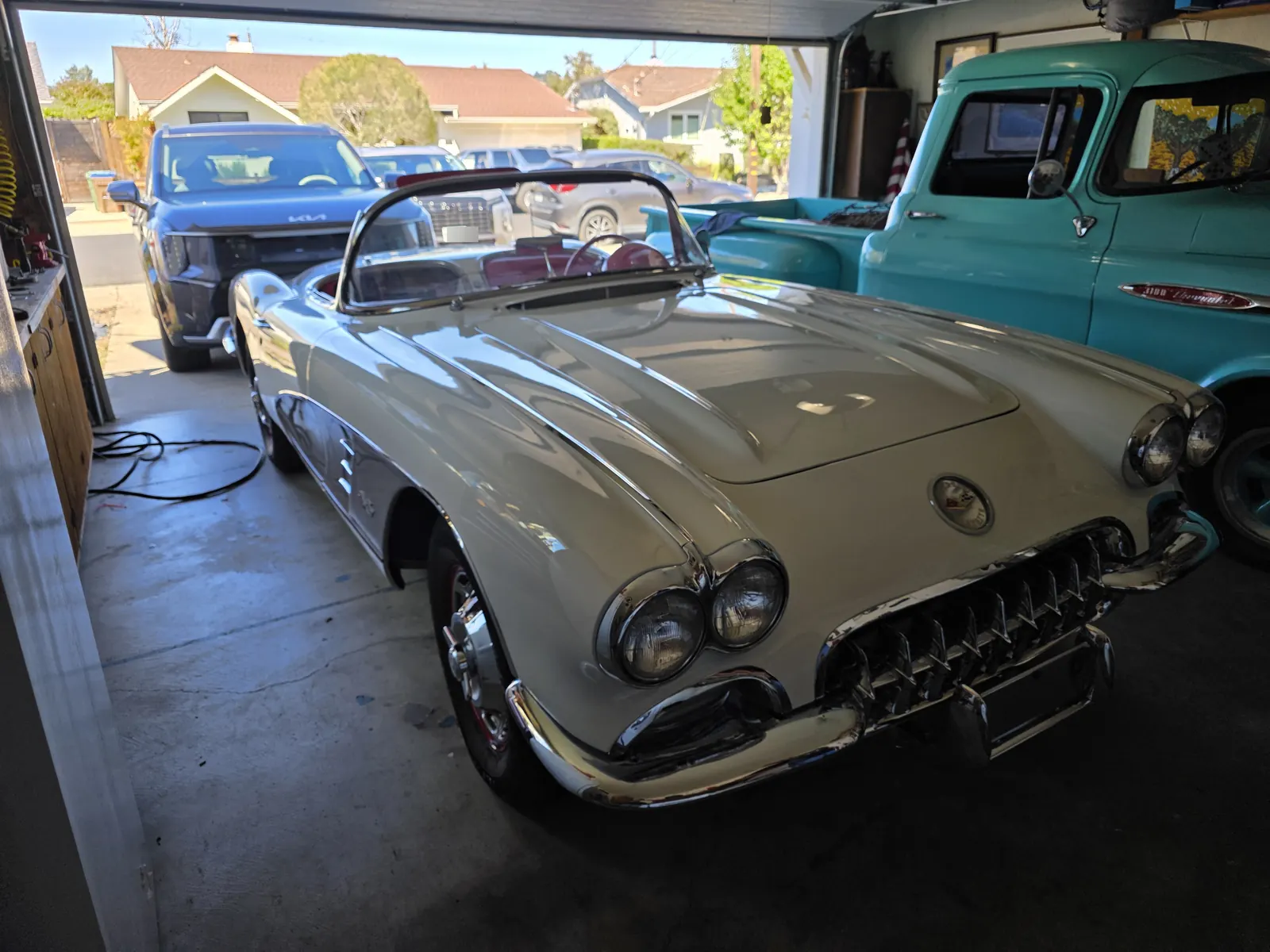 White late-1950s Chevrolet Corvette convertible in a home garage next to a turquoise vintage pickup during a mobile VIN verification.