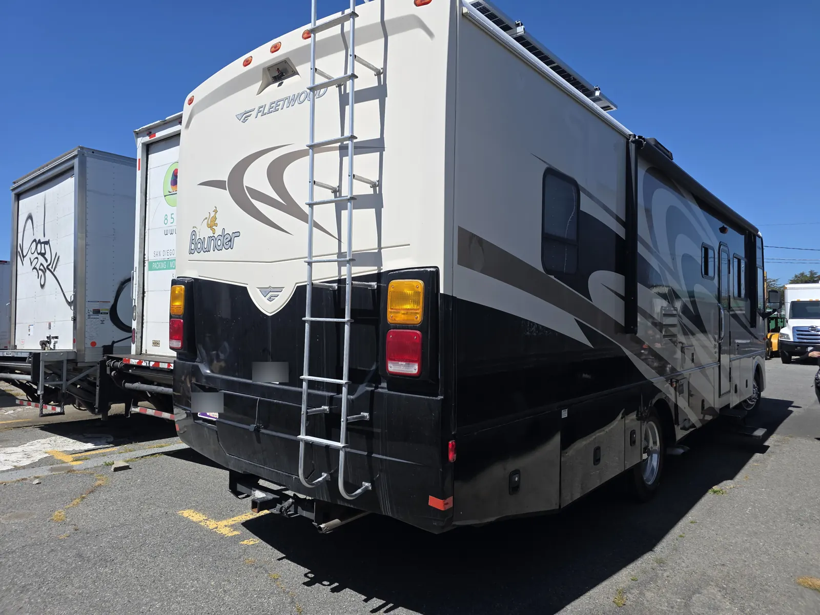 Rear three-quarter view of a Fleetwood Bounder Class A motorhome with a roof ladder, parked in a commercial lot.