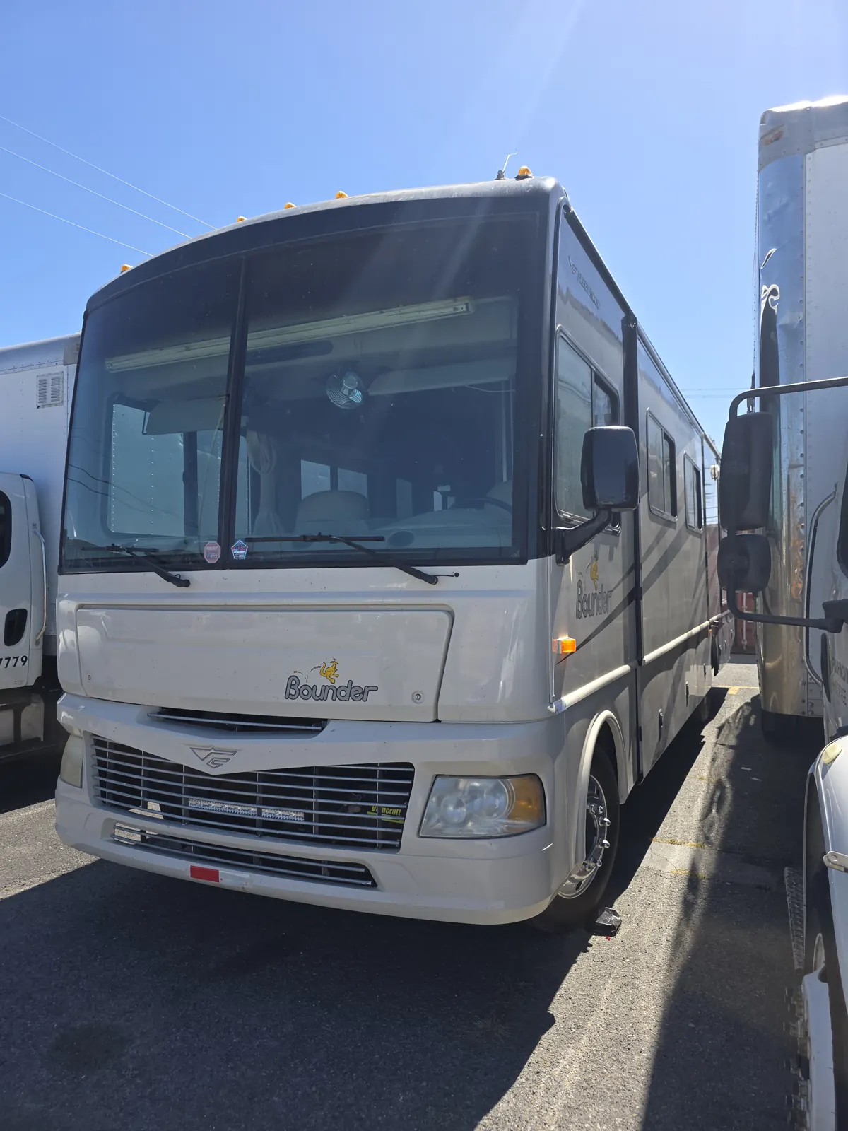 Front view of a Fleetwood Bounder Class A motorhome parked between box trucks in a storage lot.