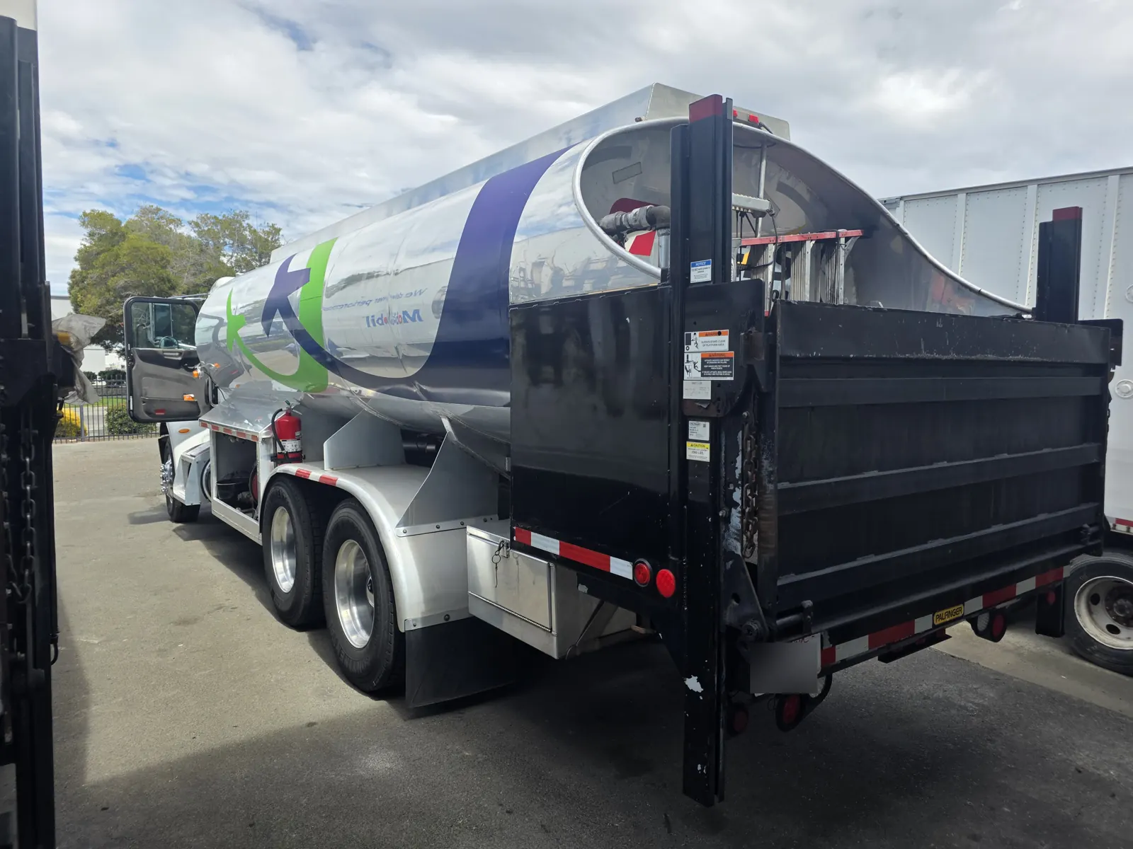 Stainless steel fuel tanker truck with a rear lift gate parked at a distribution yard during a fleet VIN verification.