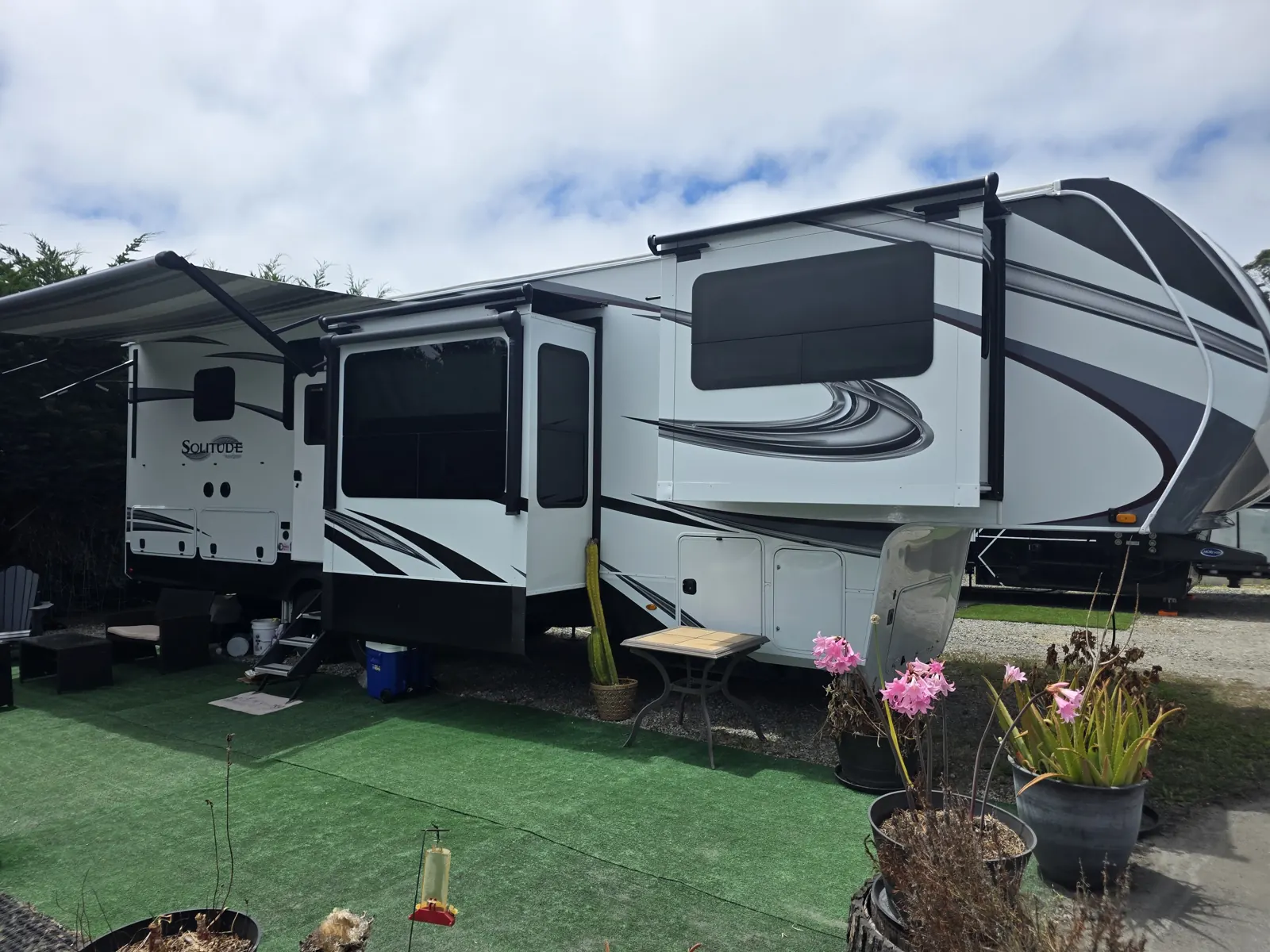 White Grand Design Solitude fifth-wheel RV with slide-outs extended, parked on a campsite pad during a mobile VIN verification.