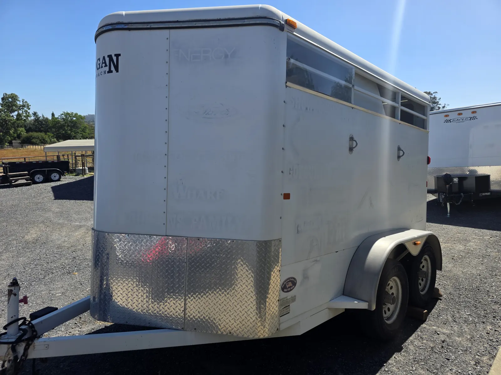 Side view of a white Logan Coach horse trailer with diamond-plate lower panels and tandem axles.