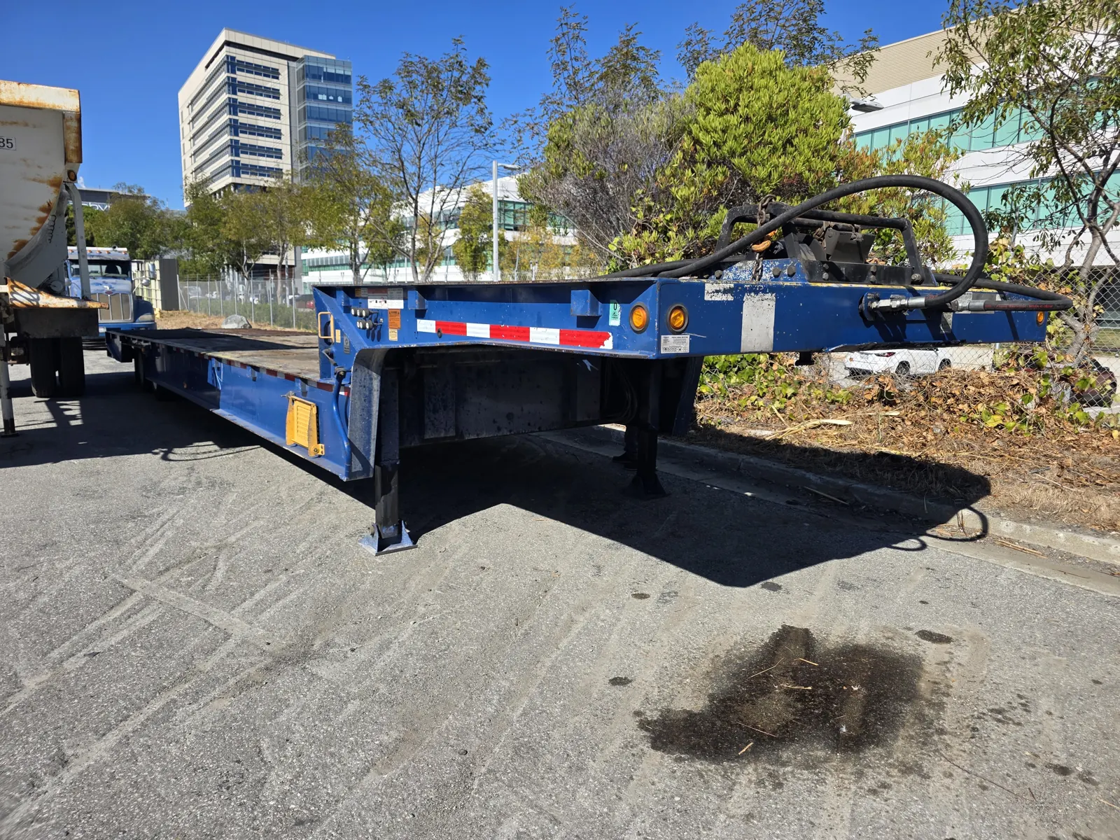 Blue hydraulic detachable-gooseneck lowboy trailer parked beside a dump truck, photographed during a commercial trailer VIN verification.