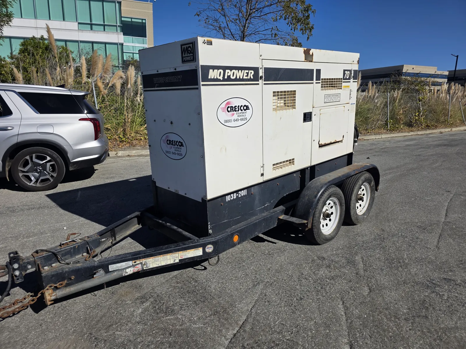 White MQ Power WhisperWatt towable generator on a black tandem-axle trailer, parked in a commercial lot for a fleet VIN verification.