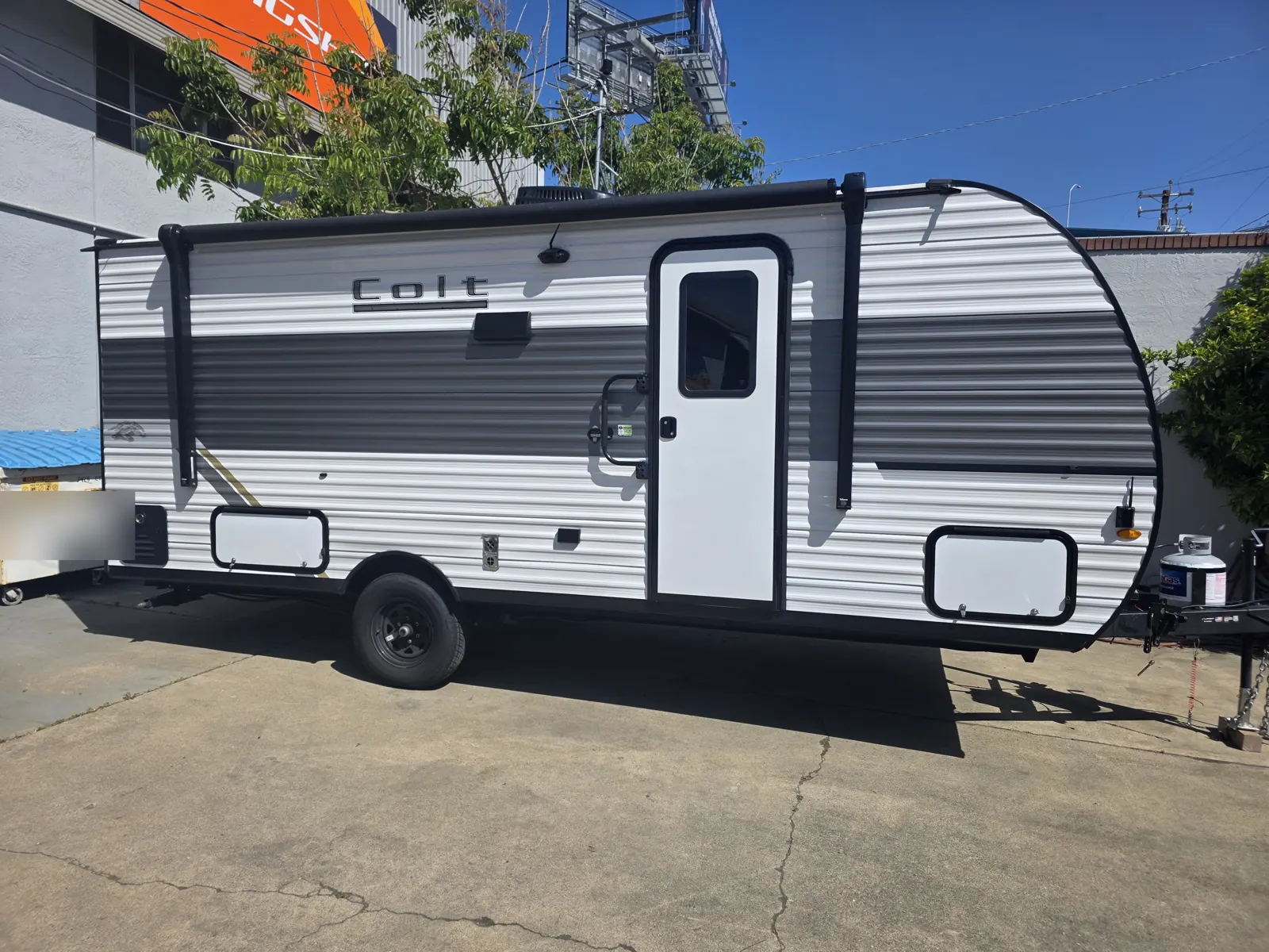 Door-side view of a white Open Range Colt travel trailer with awning retracted, parked beside a building.