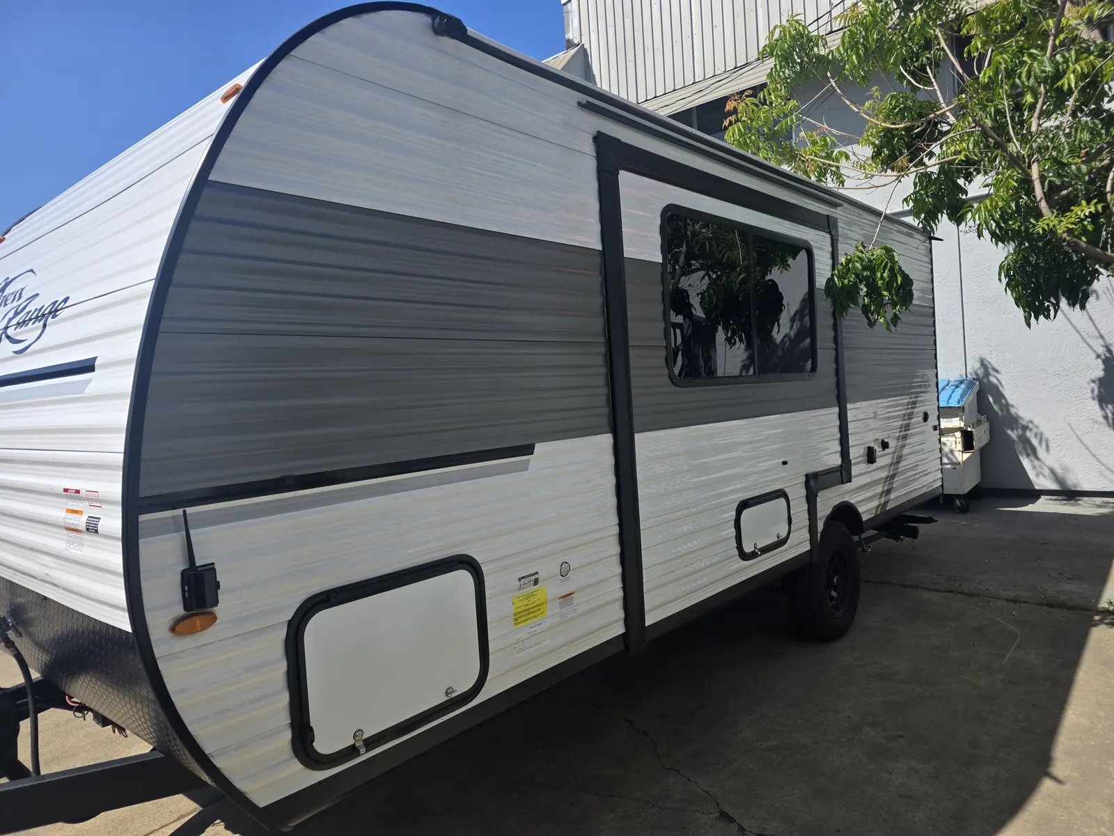 Curb-side view of a white and grey Open Range Colt travel trailer parked on a concrete pad.