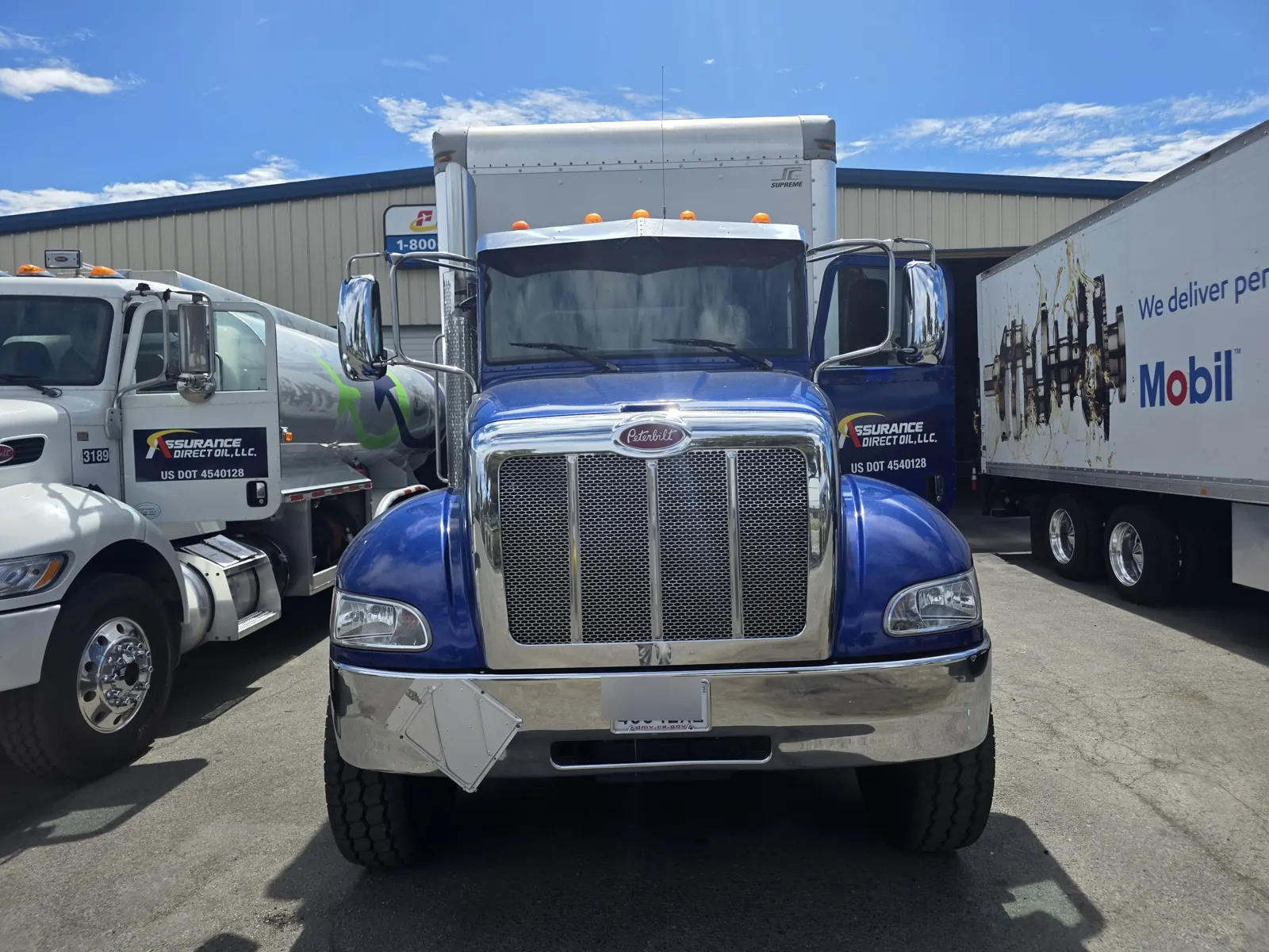Blue Peterbilt box truck with chrome grille parked between other fleet trucks for a VIN verification.
